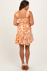 woman wearing an orange floral maternity dress with ruffle sleeves and a smocked back, showing her baby bump