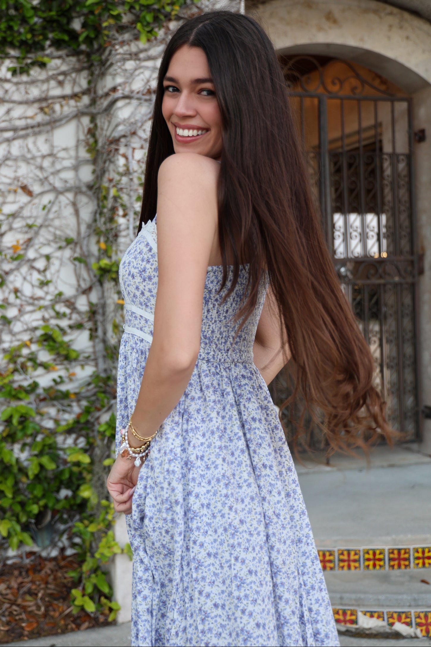 woman wearing a floral print strapless dress with a fitted bodice and flowing skirt, smiling over her shoulder