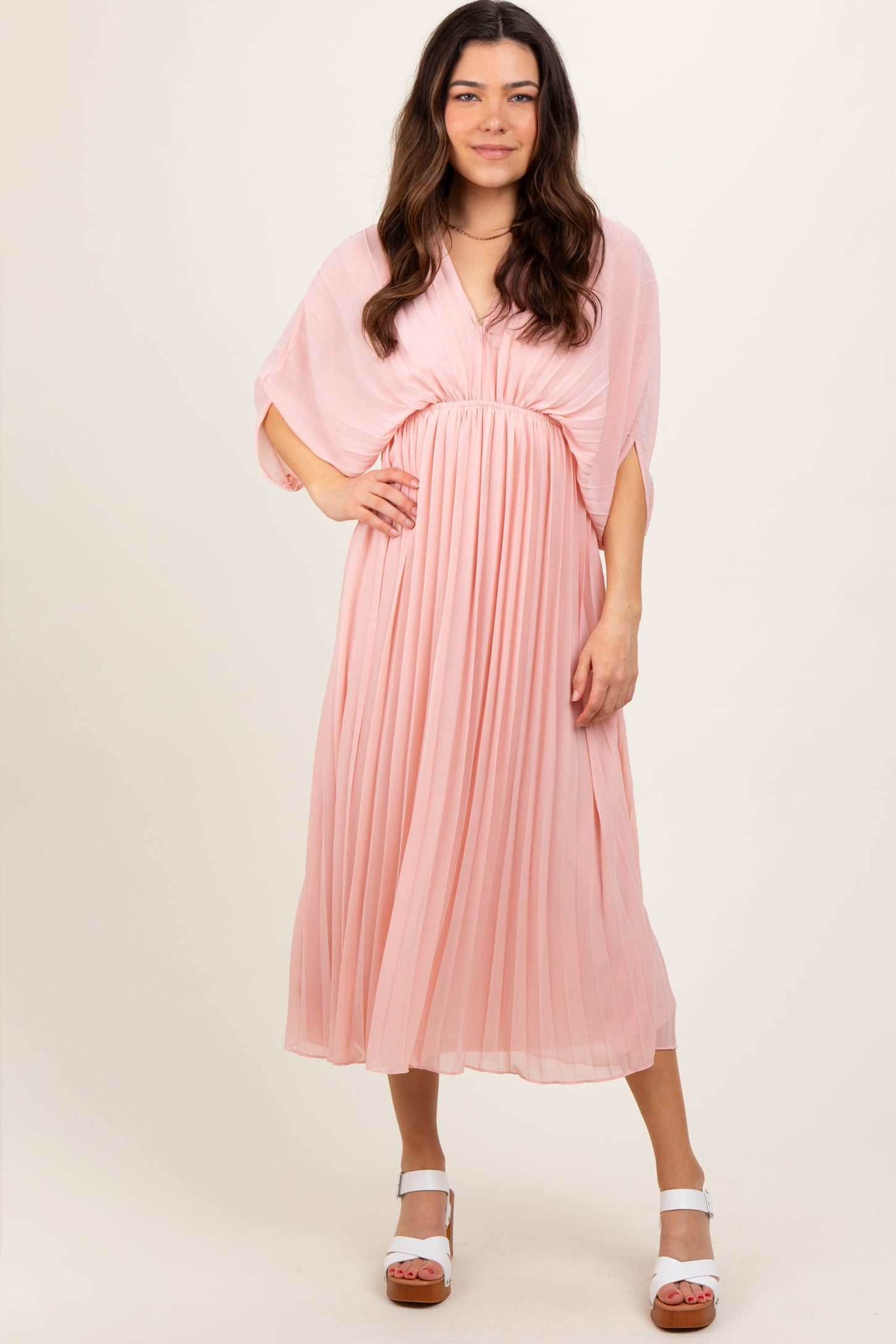 woman wearing a pink pleated maxi dress with a v-neck and flowing cape sleeves
