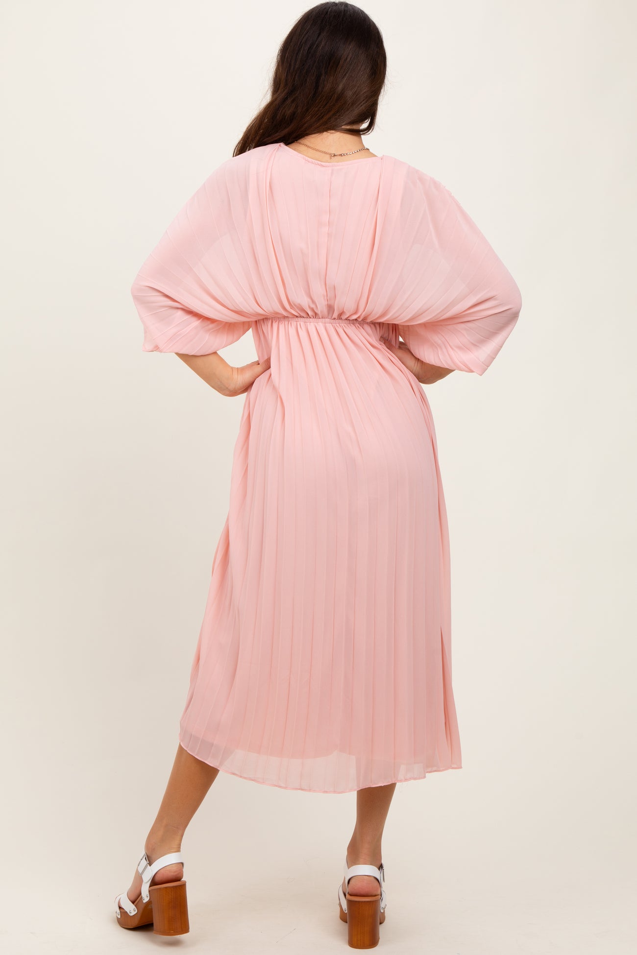 woman wearing a pink pleated midi dress with batwing sleeves, showing the back and cinched waist
