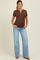 woman wearing a brown maternity henley top and light blue flared jeans, showing her baby bump