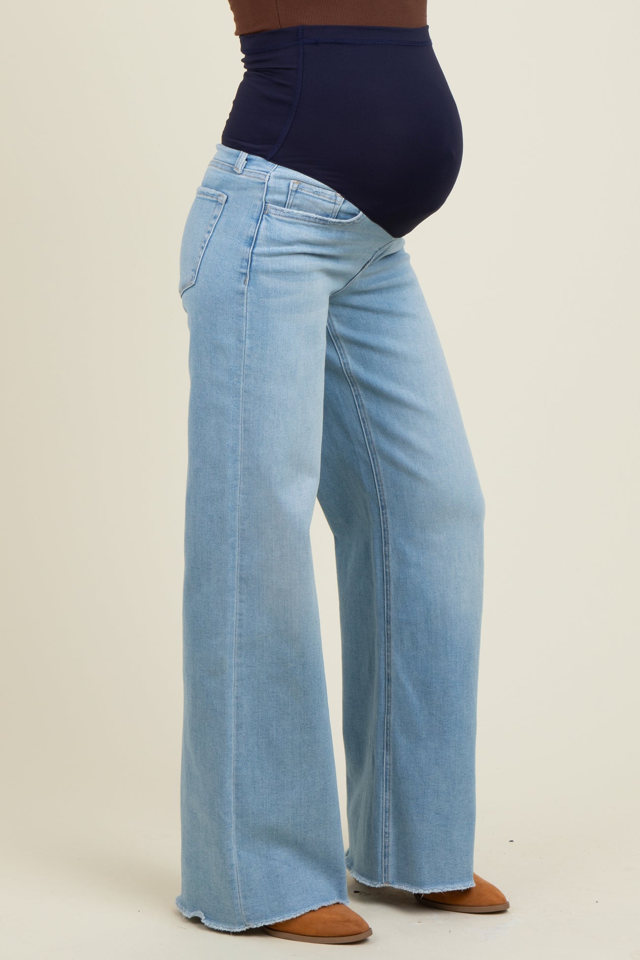 woman wearing light blue maternity jeans with a high waist and flared legs, showcasing a visible baby bump