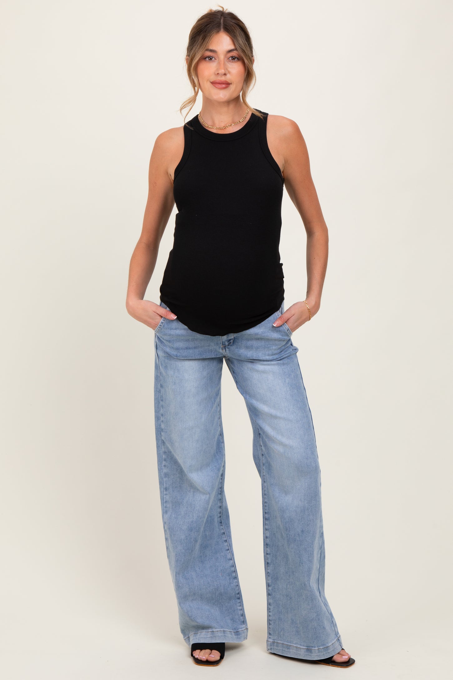 woman wearing a black ribbed maternity tank top and light blue wide-leg jeans, showcasing her baby bump