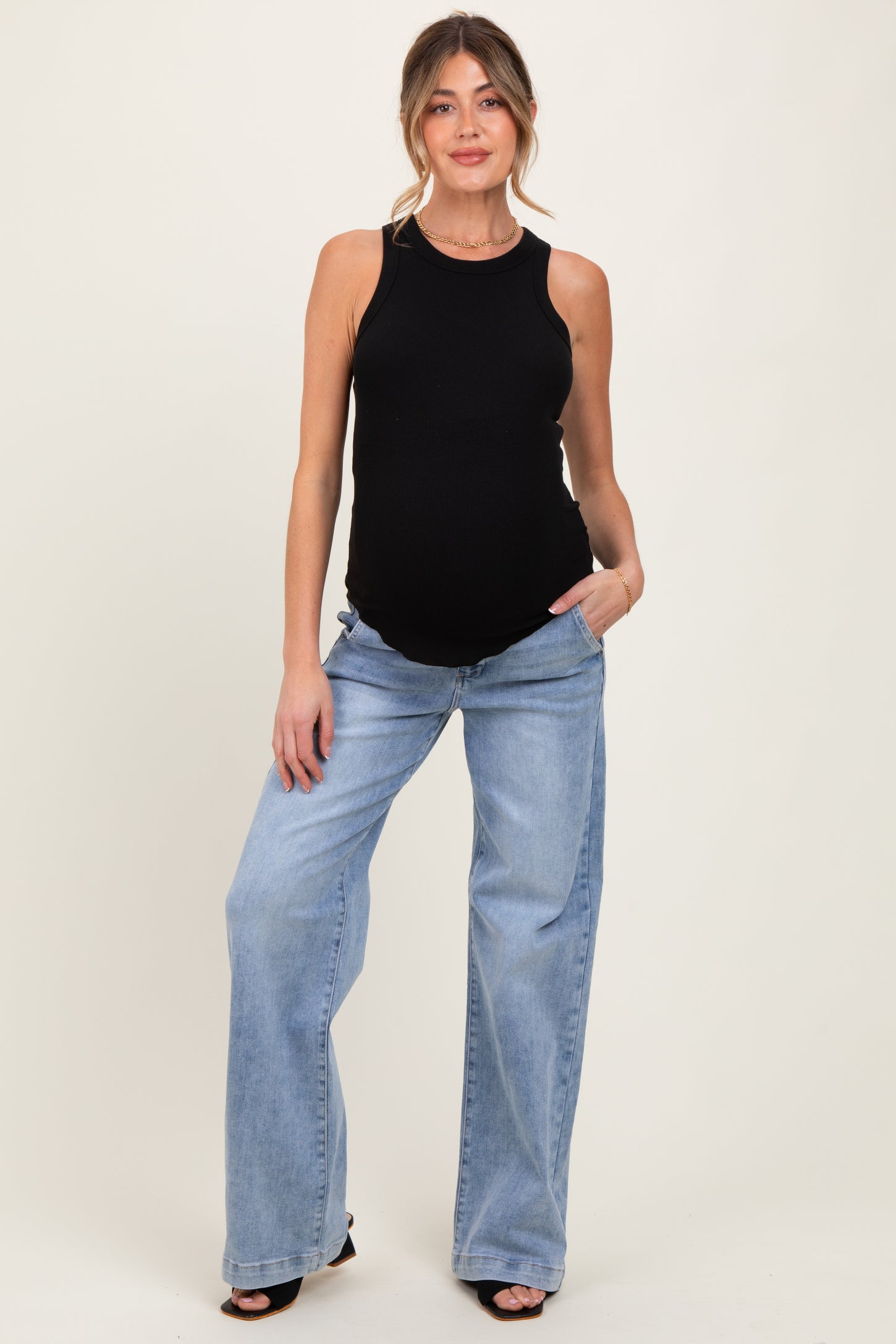 woman wearing a black ribbed maternity tank top and light blue wide leg maternity jeans with a visible baby bump