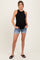 woman wearing a black ribbed maternity tank top and denim shorts, showing her baby bump and standing with hands in pockets