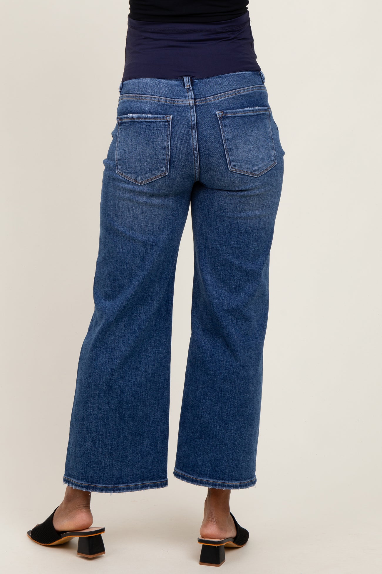 woman wearing dark blue maternity wide-leg jeans, seen from the back, with a fitted top and heeled sandals