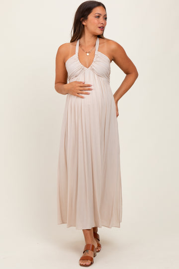 woman wearing a beige halter maternity dress, holding her baby bump, with a flowing skirt and relaxed fit