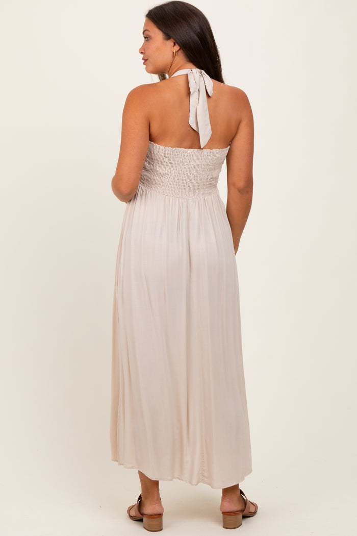 woman wearing a light beige maternity maxi dress with a smocked bodice and halter tie detail, back view