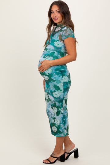 woman wearing a floral green maternity dress, hugging her baby bump, standing in side profile with a smile