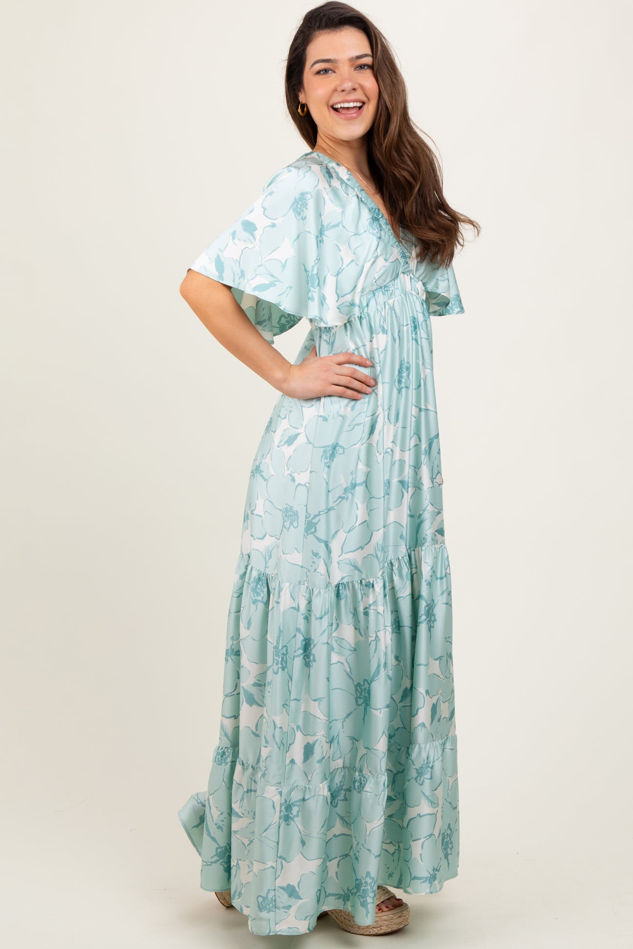 woman wearing a mint green floral maxi dress with short sleeves and a tiered skirt, standing sideways and smiling
