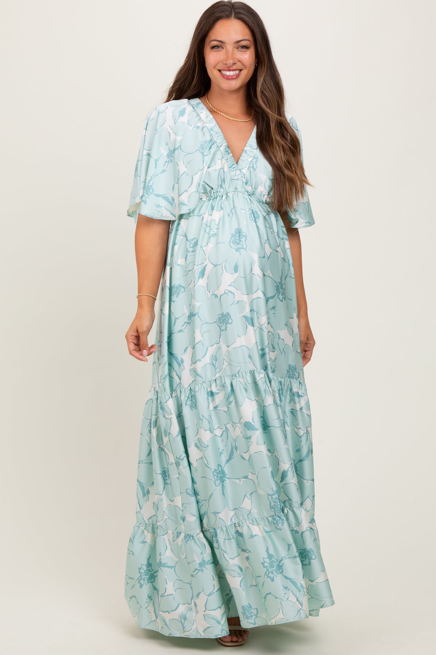 woman wearing a light blue floral maternity maxi dress with short sleeves and a tiered skirt, showcasing her baby bump