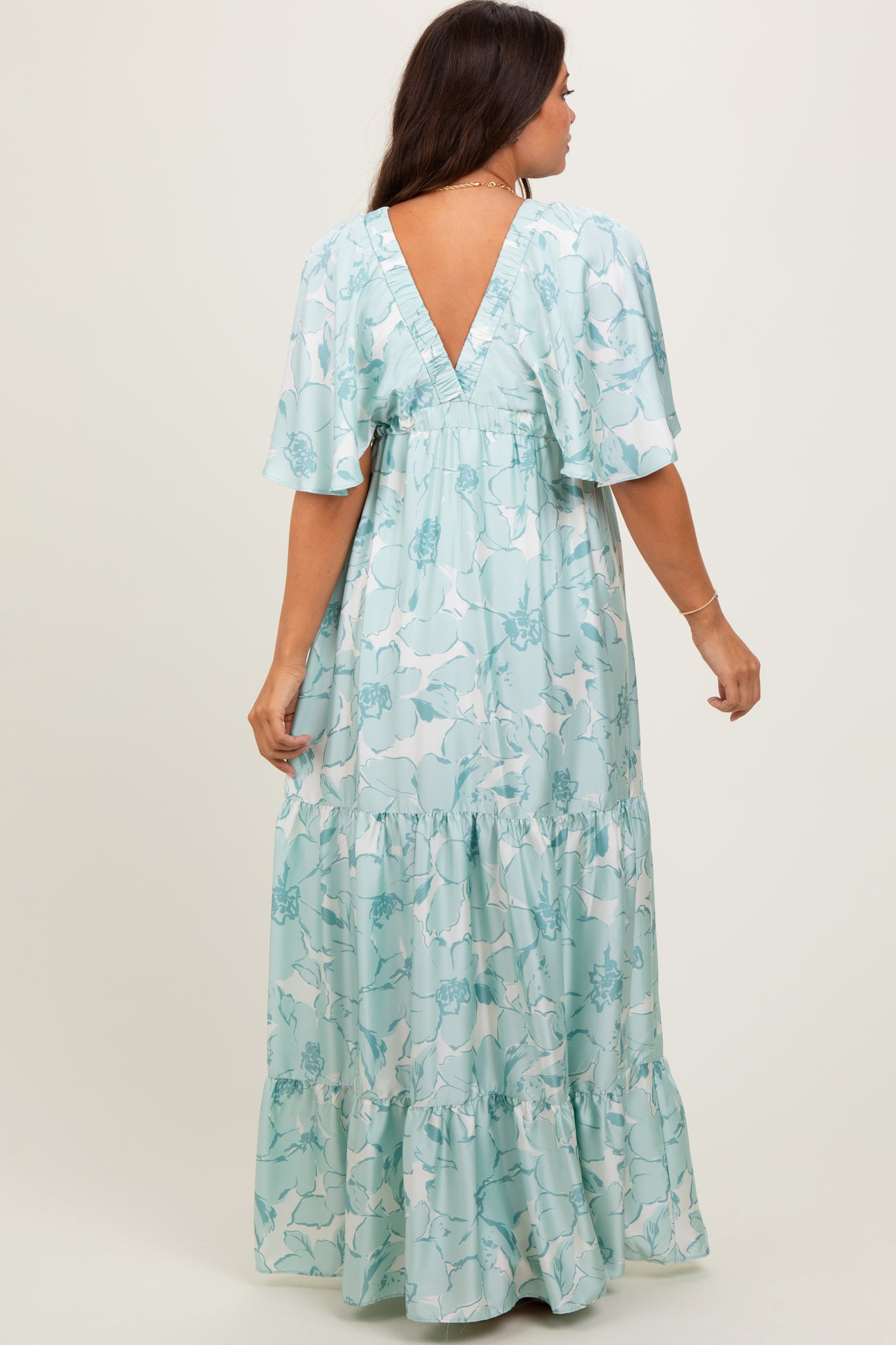 woman wearing a floral mint green maternity maxi dress with a v-back and flutter sleeves