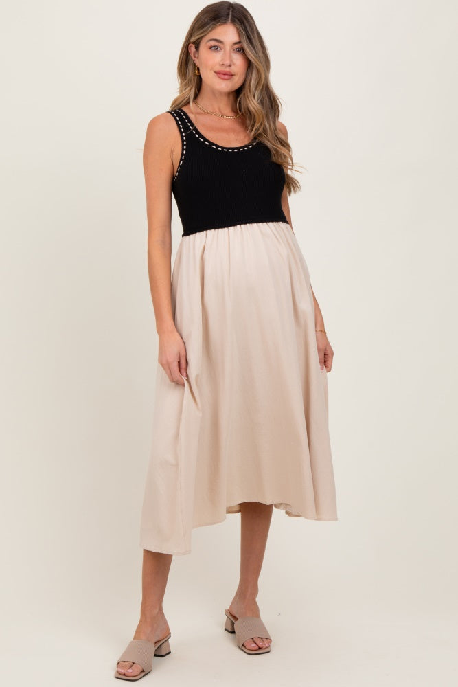 woman wearing a black and beige maternity dress with a fitted top and flowing skirt, displaying her baby bump