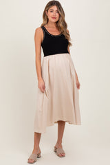 woman wearing a black and beige maternity dress with a fitted top and flowing skirt, displaying her baby bump