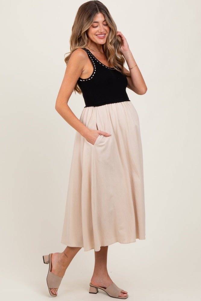 woman wearing a black maternity tank top with studded details and a tan skirt, showing a baby bump and pockets