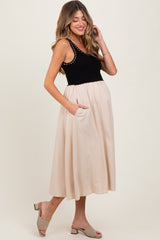 woman wearing a black maternity tank top with studded details and a tan skirt, showing a baby bump and pockets
