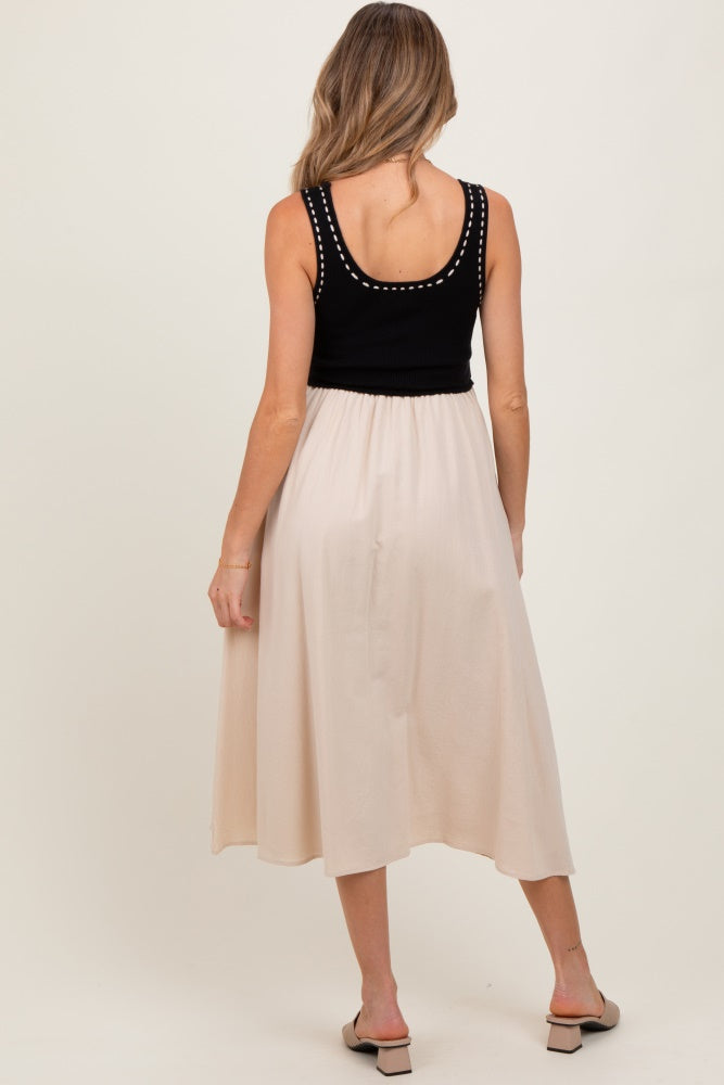 woman wearing a black sleeveless maternity top with studded details and a light beige midi skirt from the back
