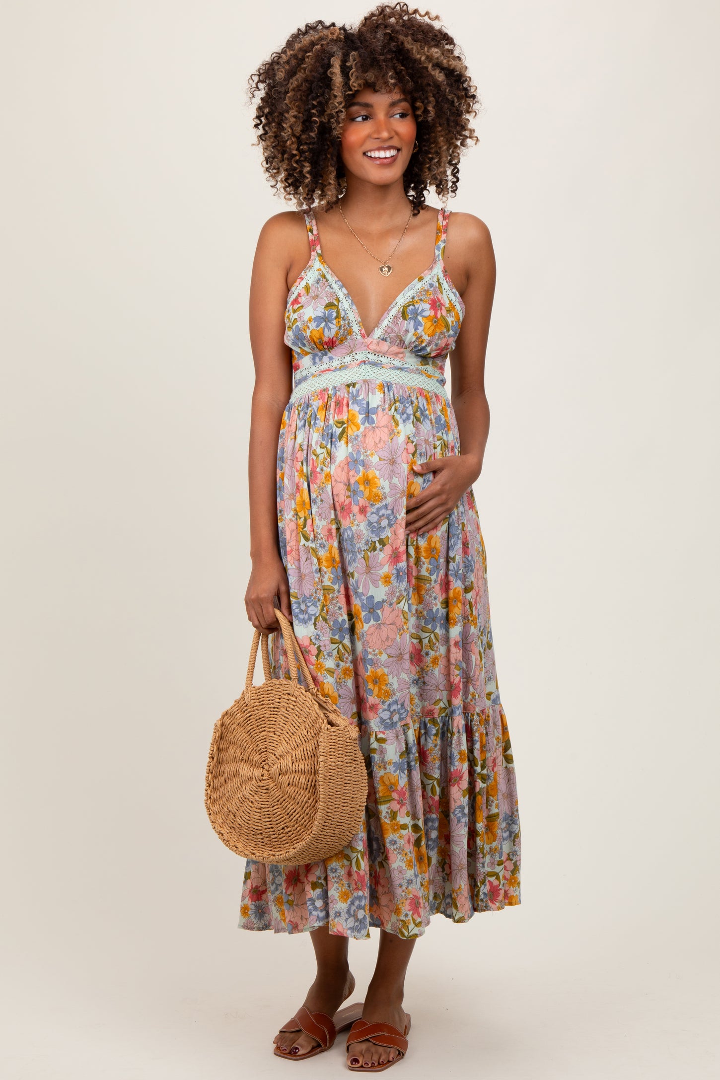 woman wearing a floral maternity maxi dress with smocked bodice and holding her baby bump while carrying a woven bag