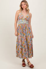 woman wearing a floral maxi dress with a v-neckline and braided details, paired with brown heeled sandals