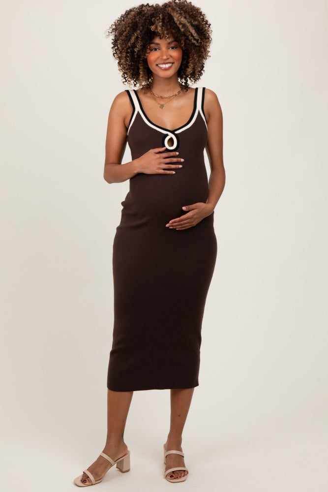 woman wearing a brown maternity dress with white detailing, holding her baby bump with a smile