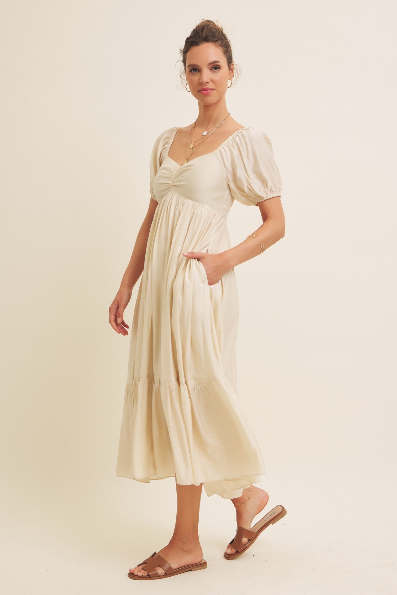 woman wearing a cream puff sleeve midi dress with a cinched waist and pockets, standing on a beige background