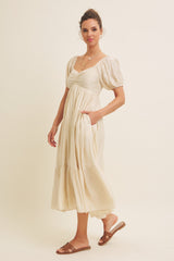 woman wearing a cream puff sleeve midi dress with a cinched waist and pockets, standing on a beige background