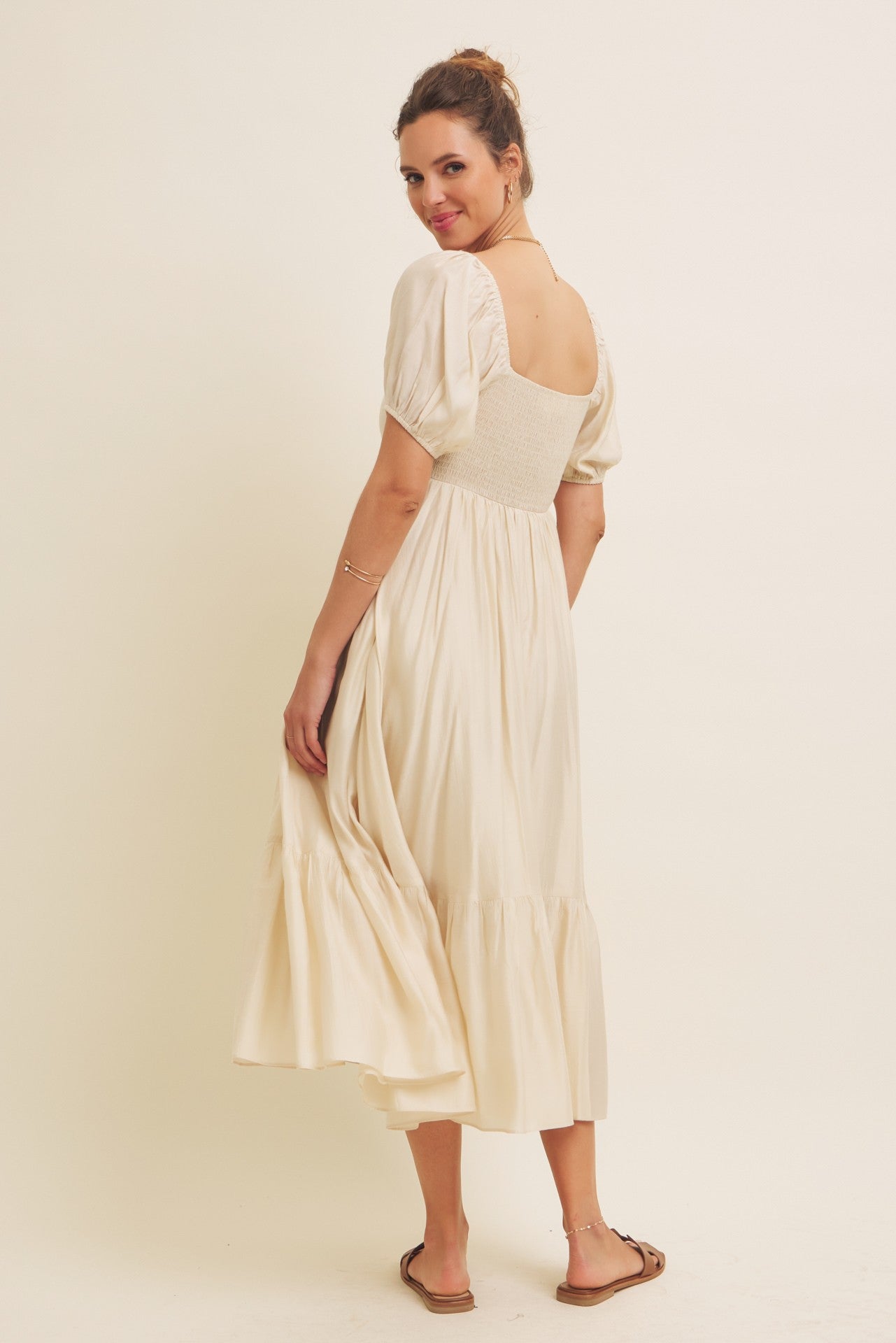 woman wearing a cream-colored midi dress with a smocked bodice and puff sleeves, standing with back to the camera