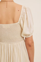 back view of a woman wearing a cream-colored dress with puff sleeves and smocked bodice detailing