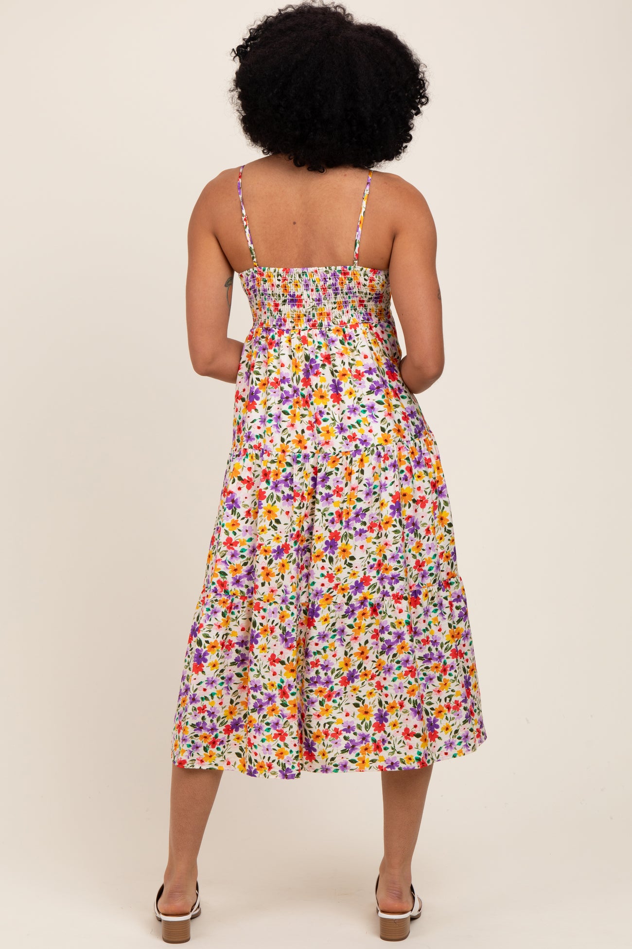 woman wearing a colorful floral midi dress with a smocked back and thin straps, standing with her back to the camera