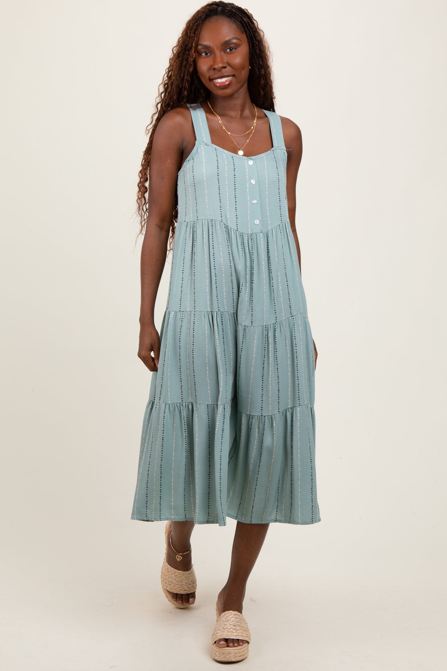 woman wearing a light teal tiered midi dress with adjustable straps and front buttons, standing with a smile