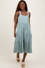 woman wearing a light teal tiered midi dress with adjustable straps and front buttons, standing with a smile