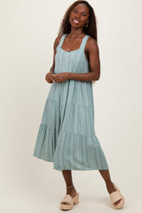 woman wearing a light blue midi dress with tiered ruffle details and buttons, standing in a relaxed pose