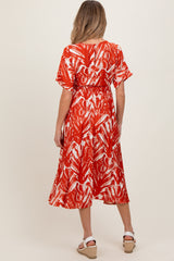 woman wearing a red and white patterned maternity dress with short sleeves and a cinched waist, facing away from the camera