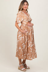 woman wearing a brown and white leaf print maternity dress with a tied waistband and pockets, holding her baby bump