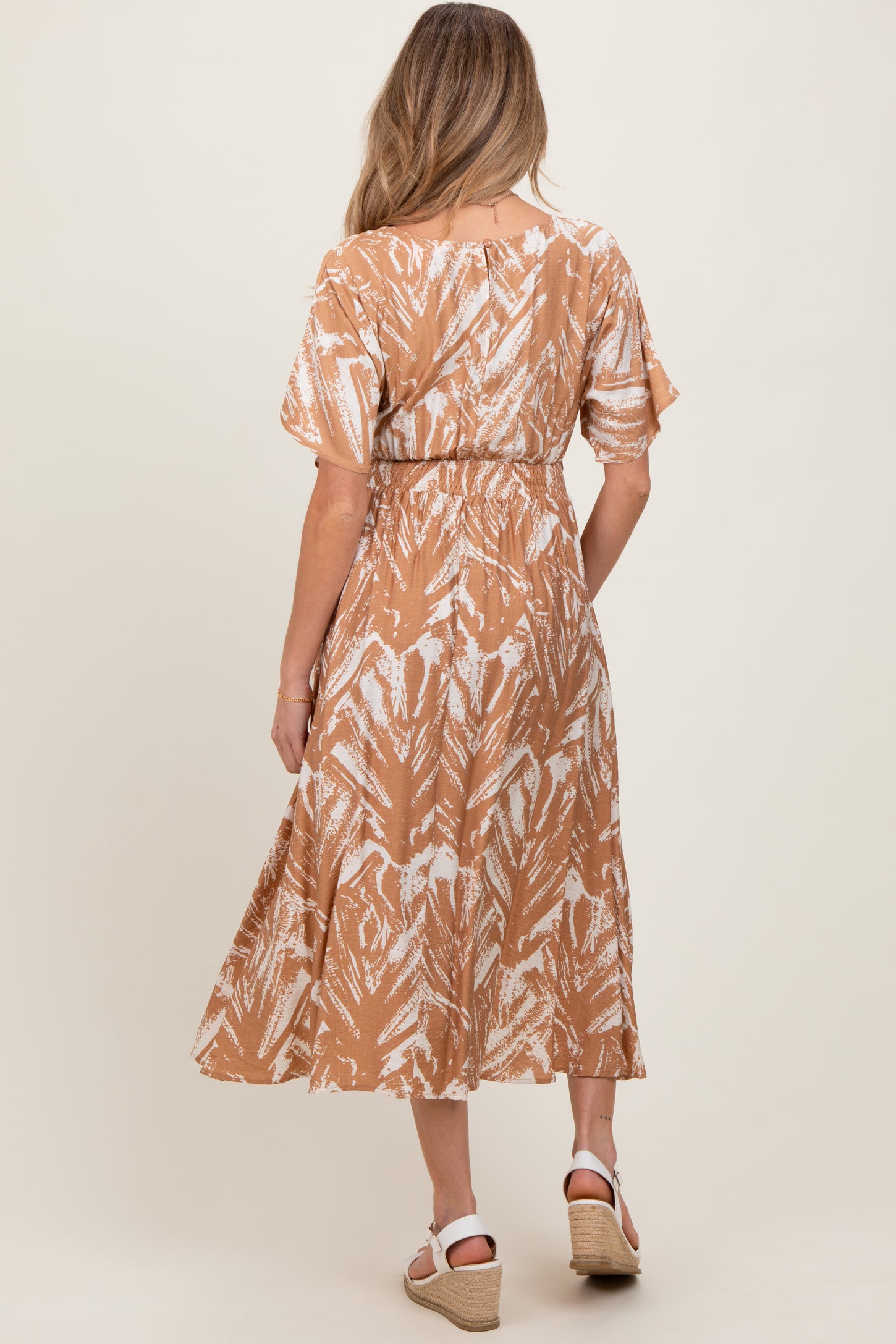 woman wearing a brown and white floral print maternity dress with short sleeves and a cinched waist, showing her baby bump
