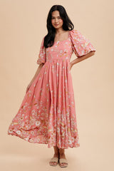 woman wearing a pink floral maxi dress with puff sleeves and a square neckline, standing against a neutral background