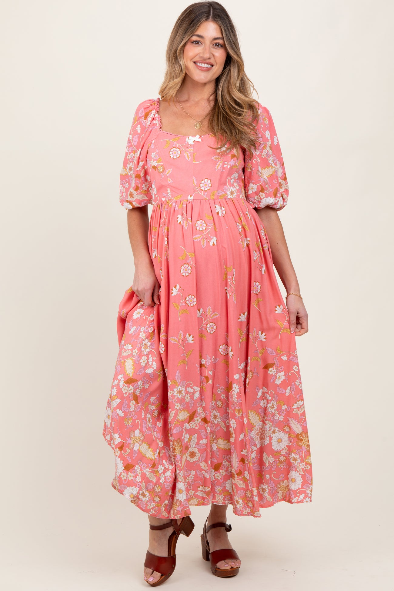 woman wearing a pink floral maternity dress with puff sleeves and a flowing skirt, showing her baby bump