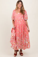 woman wearing a pink floral maternity dress with puff sleeves and a flowing skirt, showing her baby bump