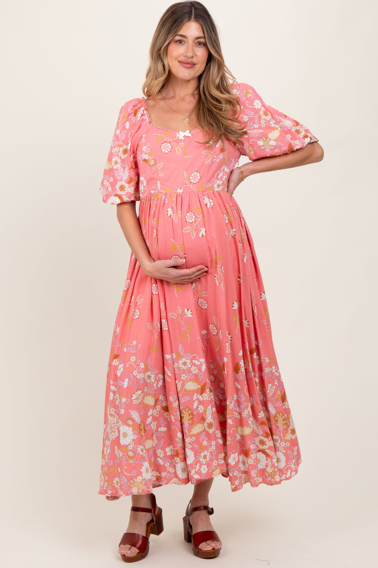 woman wearing a pink floral maternity maxi dress and holding her baby bump