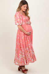 woman wearing a pink floral maternity dress with puff sleeves and a flowing skirt, gently cradling her baby bump