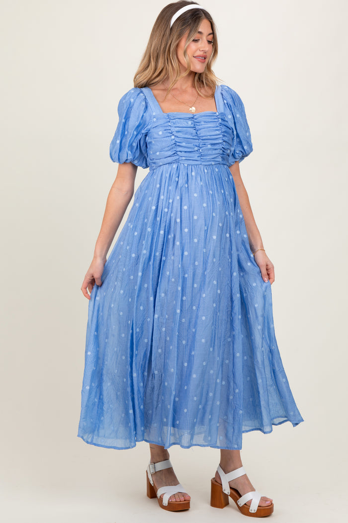 woman wearing a light blue maternity dress with puff sleeves and polka dot details, showing her baby bump