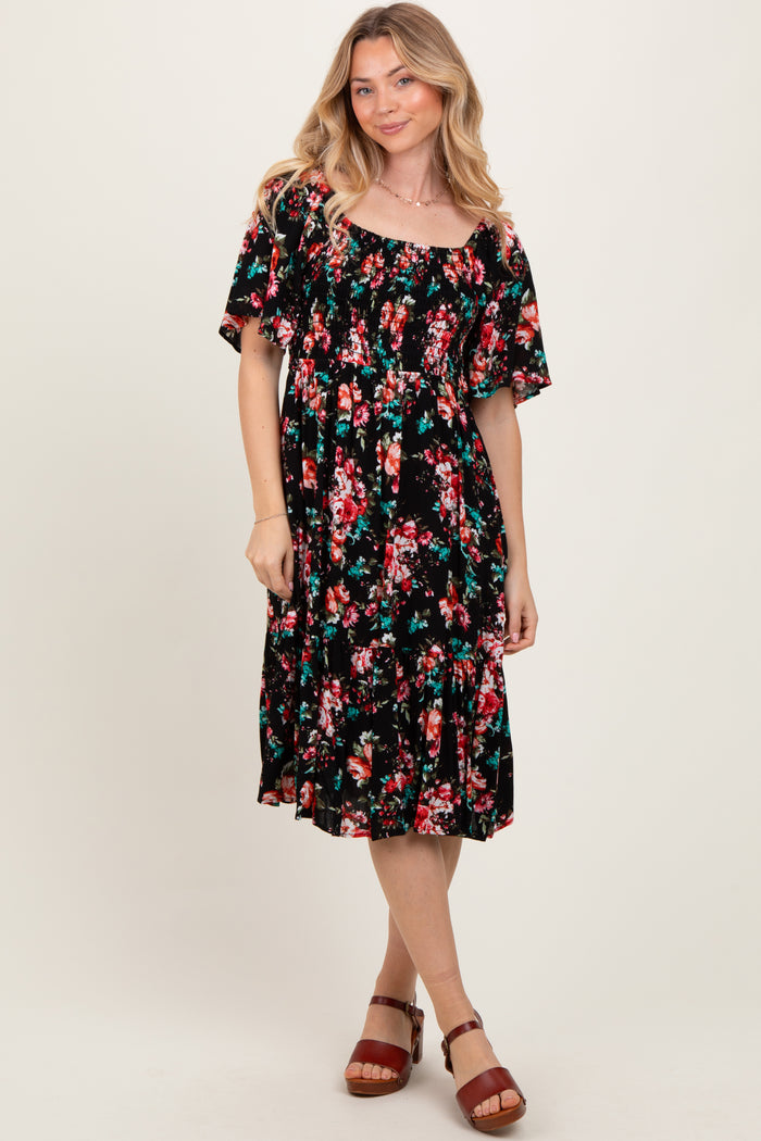 woman wearing a black floral midi dress with short sleeves and a gathered waist, standing and smiling