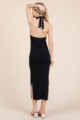 woman wearing a black halter neck midi dress with ruching and a side slit, viewed from the back