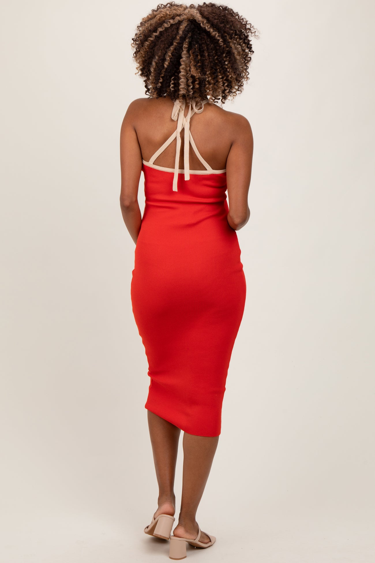 woman wearing a red halter neck maternity dress with a fitted silhouette and mid-length hem, showing her back