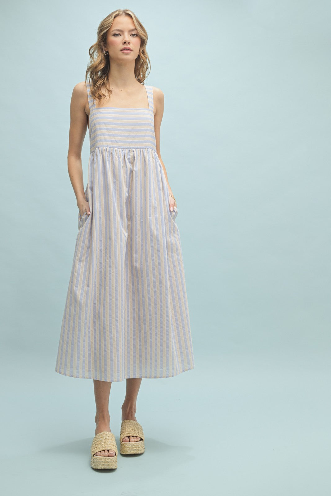 woman wearing a striped midi dress with a square neck, spaghetti straps, and pockets