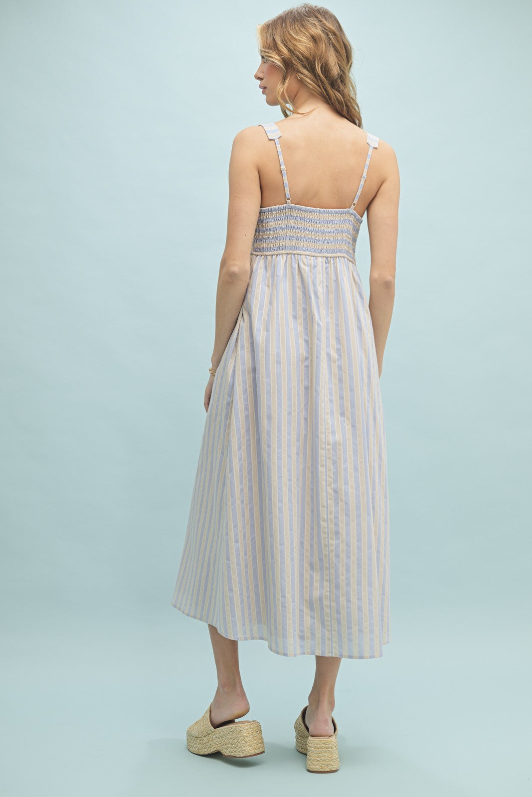 woman wearing a light blue and white striped midi dress with smocked back and thin shoulder straps