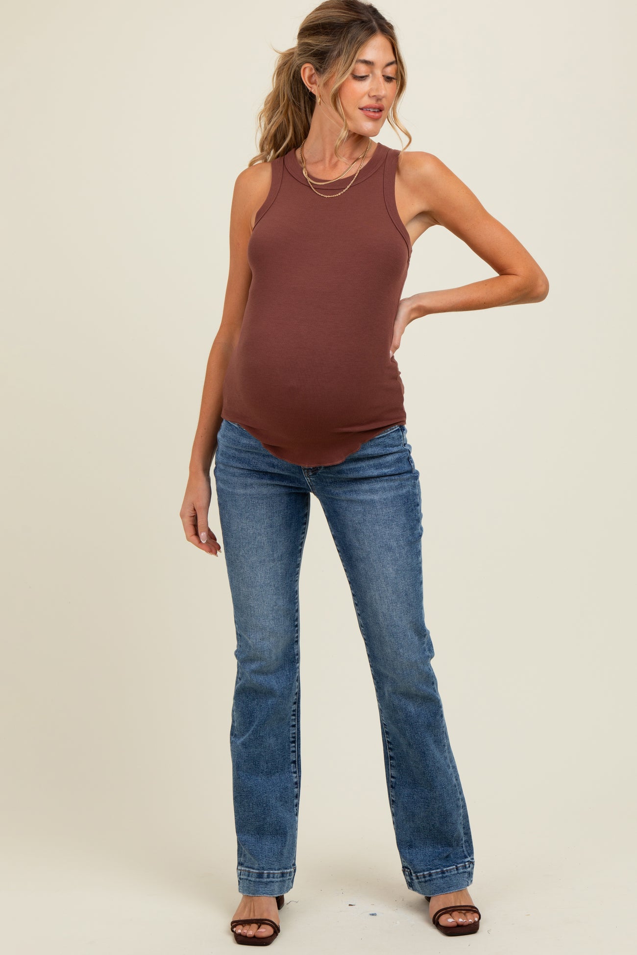 woman wearing a brown maternity tank top and blue flared jeans, showing a visible baby bump