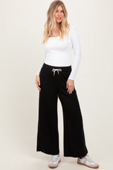 woman wearing a white long sleeve fitted top and black wide-leg sweatpants with a drawstring waist