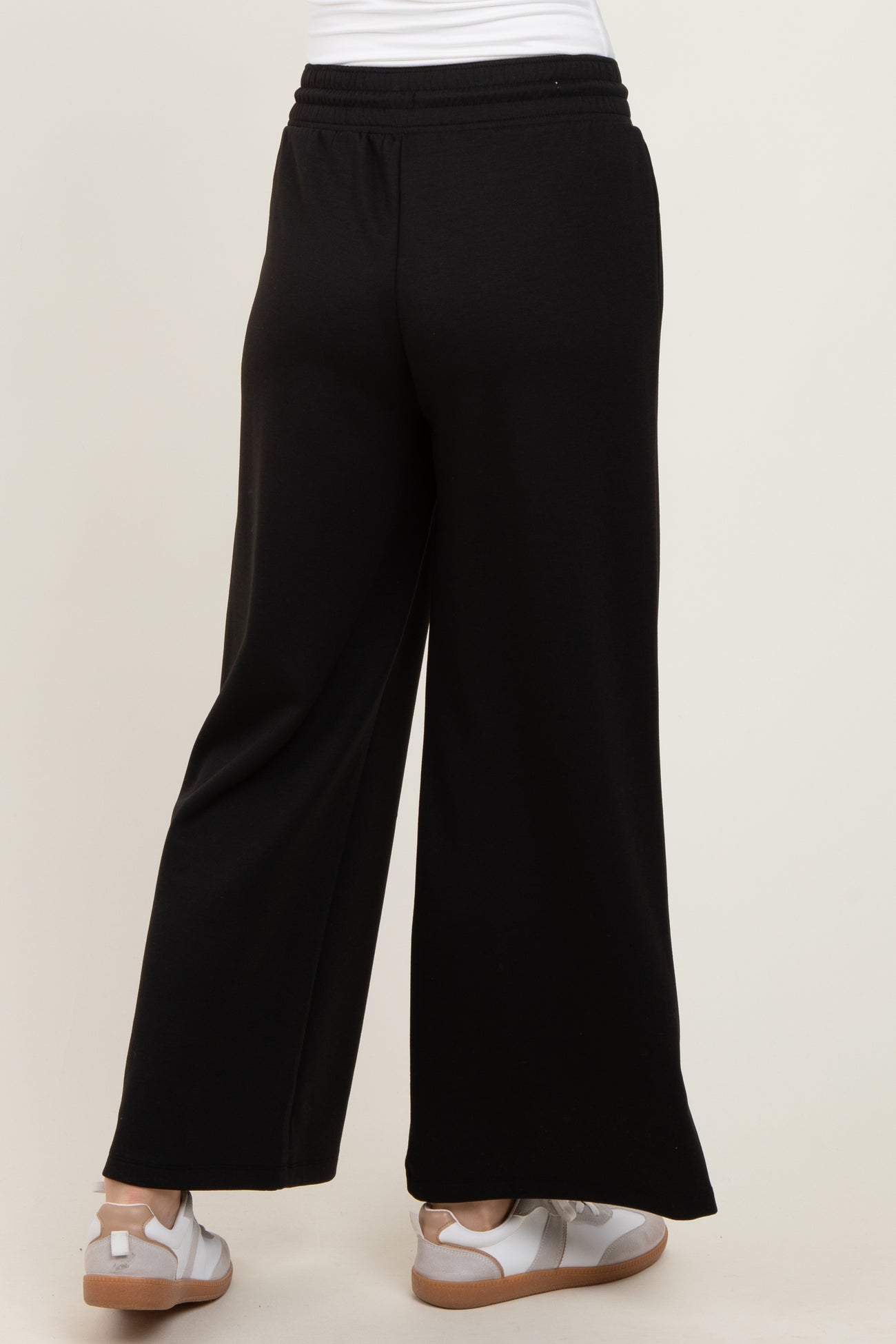 woman wearing black wide-leg pants, viewed from the back, paired with white sneakers