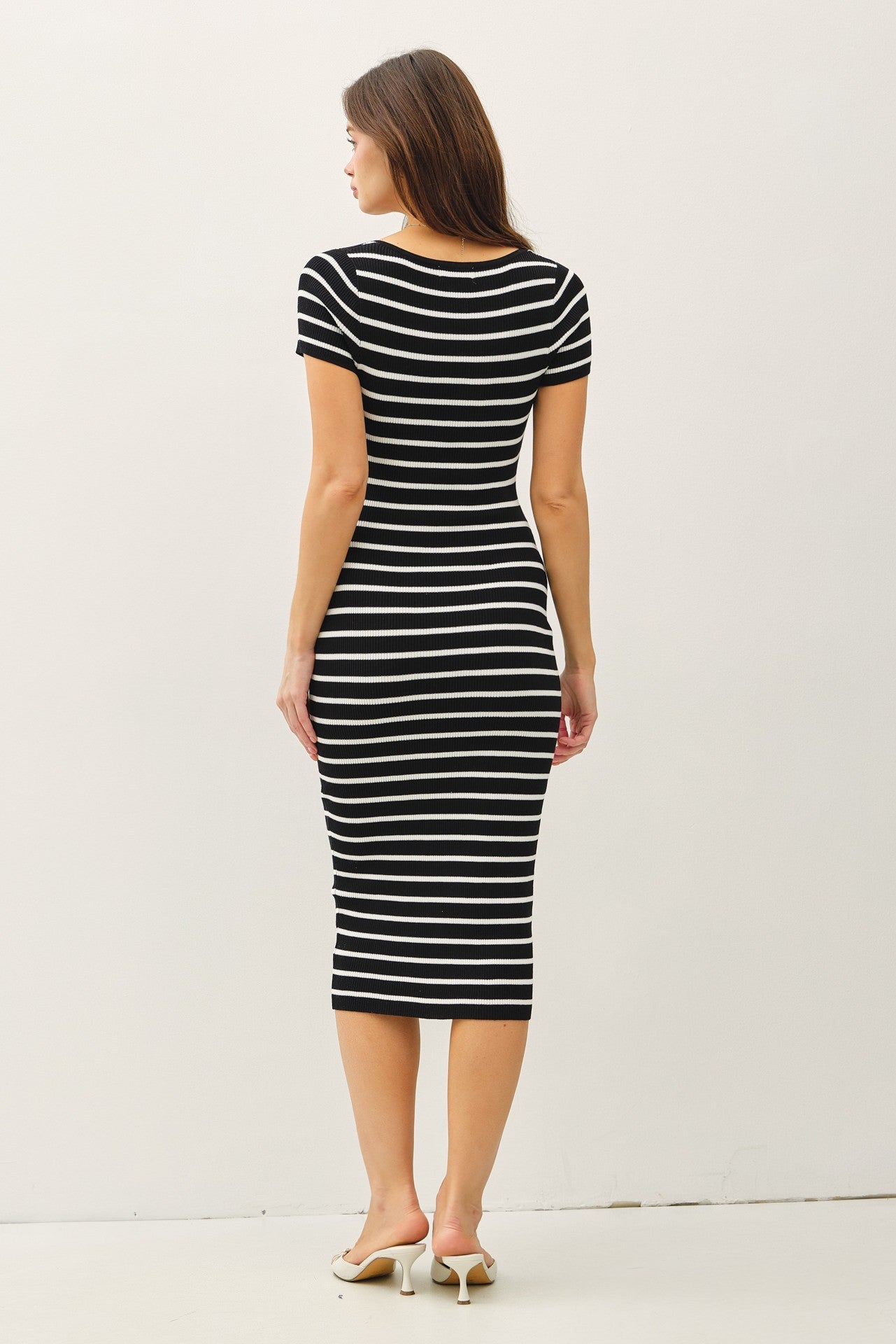 woman wearing a black and white striped fitted midi dress while standing with her back to the camera